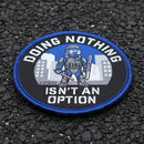 A circular embroidered patch with a blue border and the text 'DOING NOTHING ISN'T AN OPTION' around a graphic of a tactical officer in front of city buildings. The patch is placed on tarmac