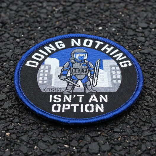 A circular embroidered patch with a blue border and the text 'DOING NOTHING ISN'T AN OPTION' around a graphic of a tactical officer in front of city buildings. The patch is placed on tarmac